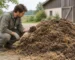 Una persona è accovacciata accanto a un cumulo di letame di stalla scuro con paglia e osserva una manciata di materiale.